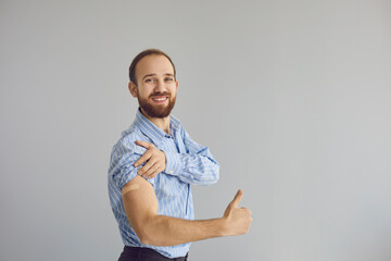 Vaccination campaign. Adult caucasian business man office worker showing medical adhesive patch on arm after receiving COVID vaccine gesturing thumbs up and smiling to camera expressing studio shot