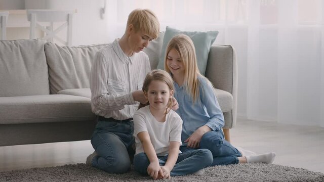 Happy Mom Talking With Daughters And Braiding Hair At Home
