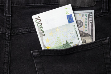  One hundred euro and one hundred dollar bills sticking out of the pocket of black jeans