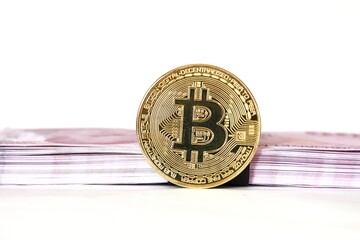 Gold color bitcoin in front of stack of money banknotes isolated on white background. The popular cryptocurrency is bitcoin.