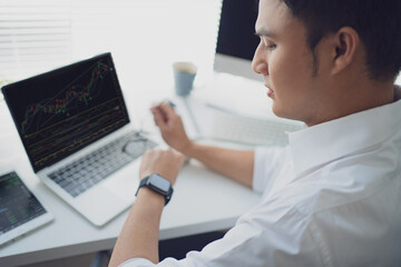 Young man trades stocks on a laptop screen. He was looking at the watch on his wrist.