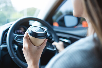Closeup image of a woman holding and drinking coffee while driving a car