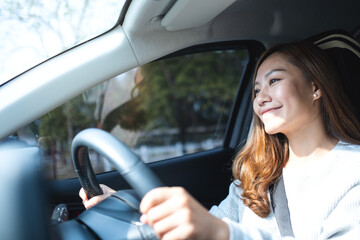 A beautiful young asian woman holding steering wheel while driving a car