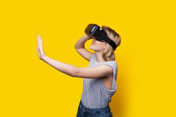 Blonde woman with virtual reality headset is touching something on a yellow studio wall