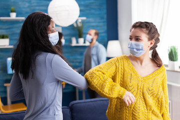 Cheerful african woman and her friend touching elbow keeping social distancing while greating each other wearing face mask, to prevent coronavirus spread in the course of global pandemic in living