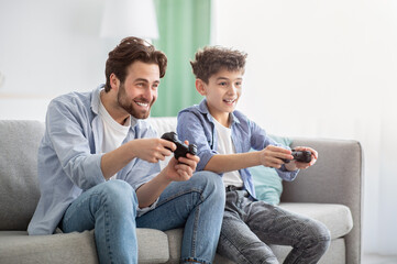 Boys are boys. Joyful father and teen son competing with each other in online video games, using...