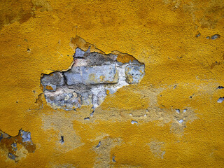 Empty textured yellow plaster wall with old bricks behind