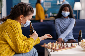 Friends with protection masks relaxing playing chess while drinking beer, clinking bottles...