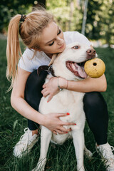 Caucasian woman and her labrador are playing in a park on the grass with a toy ball