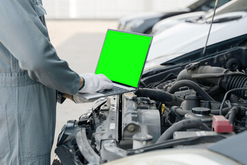 Mechanic using a laptop computer green screen to check collect information during work a car engine. service maintenance of industrial to engine repair.