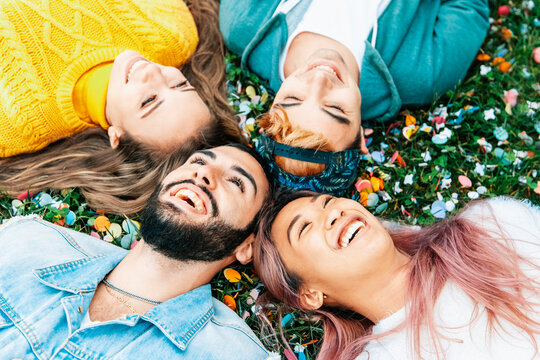 Group of multiracial friends having fun together lying on the grass - Young people laughing outdoor - Friendship concept with guys and girls on vacation - Powered by Adobe