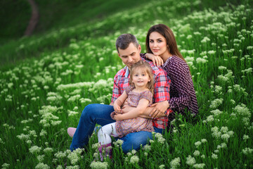 Naklejka na ściany i meble young family is sitting on the green grass. flowers bloom around