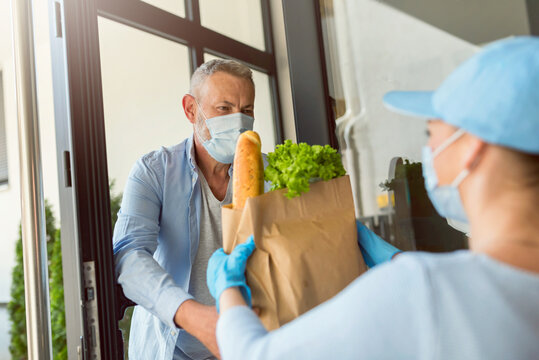 Delivery Service Girl Brings Groceries To An Elderly Man During The COVID Pandemic. Everybody Wearing Protective Masks.