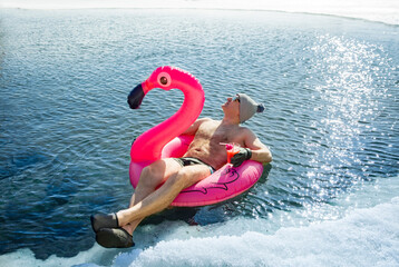 A man swimming in an ice hole in winter in Finland, floating on a pink inflatable flamingo with...