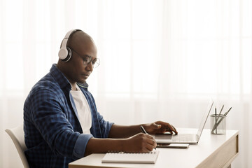 Concentrated african american mature freelancer working with laptop computer from home office, copy...