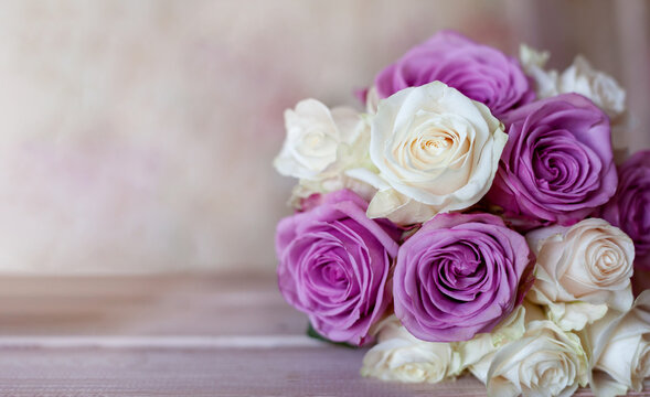 A bouquet of white and purple roses lies on a wooden table. Copy space