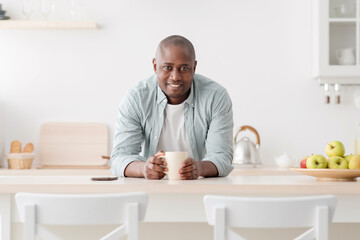 Harmony of life. Happy african american mature man drinking coffee at home in the kitchen, looking at camera and smiling