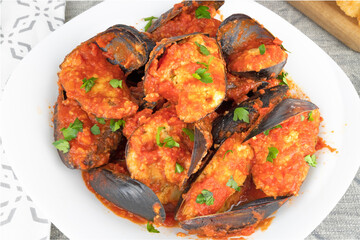 Stuffed mussels with tomato sauce and parsley on the white plate.
