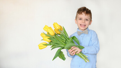 Portrait of a little boy kid holding a bouquet of yellow tulips and smile.