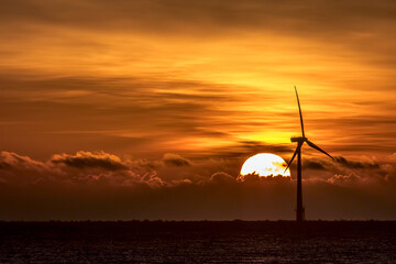 Tropical sunset background image with wind turbine on sea horizon. Dark eco-tourism background image at dusk