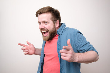 Funny bearded man in casual clothes makes a gesture with hands, smiles broadly and looks slyly at the camera. White background.