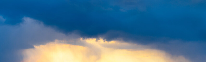 Naklejka na ściany i meble Panorama of the evening blue sky with dark and light clouds illuminated by the sun