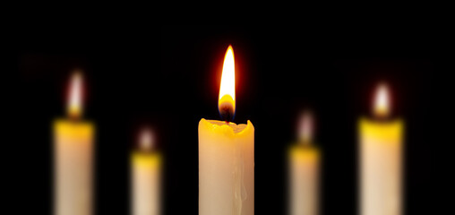 Row of candles on a black background. Candles are burning