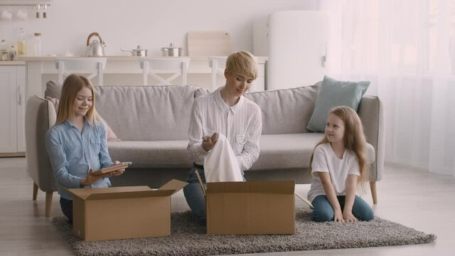 Mother And Daughters Unpacking Boxes With New Clothes At Home