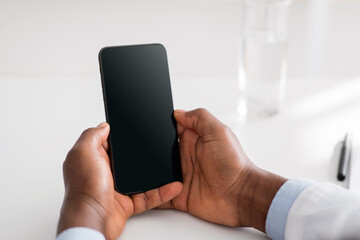 Online doctor and remote advice. Black male doctor using smartphone with blank screen, consulting patients distantly