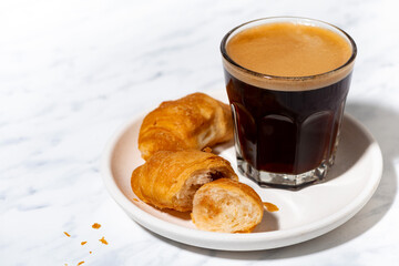 black coffee in a glass and mini croissant, top view