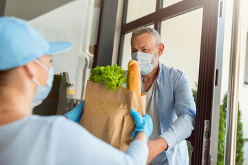 Delivery service girl brings groceries to an elderly man during the COVID pandemic. Everybody wearing protective masks.