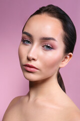 Portrait of young beautiful woman with perfectly clean face skin wearing professional make up. Female with long black hair tied in a ponytail. Close up, copy space background.
