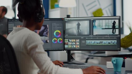 African video editor working with footage and sound, editing new project cutting film montage sitting in modern agency office. Woman using computer processing movie in post production software