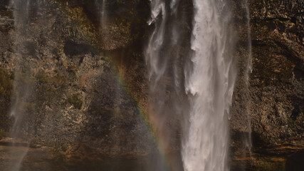Closeup view of famous waterfall Seljalandsfoss, a popular tourist destination in the south of Iceland near ring road, on sunny winter day with beautiful rainbow in front of rugged rock.