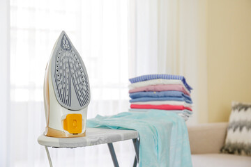 Neat stack of clean freshly laundered clothes and electric iron on pressboard at home. Pile of...