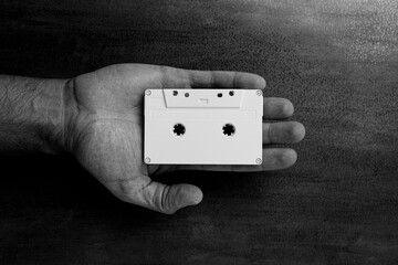 There is a white audio magnetic cassette in the man's hand. Below is a wooden background. Black and white