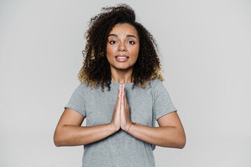 The curly-haired woman asking for something with palms to each other while standing in the studio