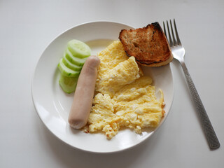 Sausage, scrambled eggs, toast and cucumber on a white plate, fork nearby. White background