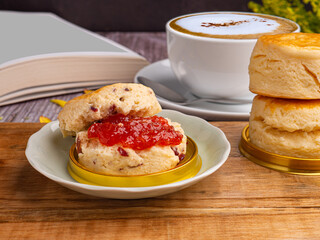 Scones traditional English delicious freshly baked homemade with strawberry jam and served on a wooden tray with a coffee cup. Side view. Dessert, beverage, and relaxation concept