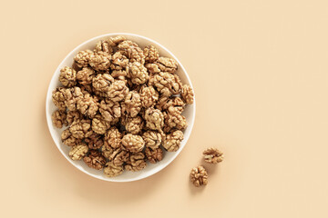 Healthy walnuts without shells in white plate on beige background with copy space. View from above.