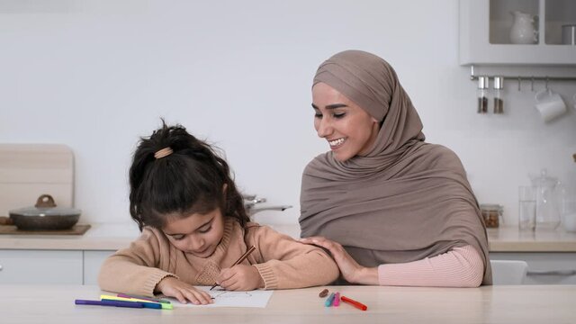 Cheerful Muslim Mom And Daughter Drawing Together Sitting In Kitchen