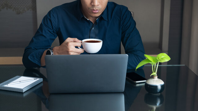 Business man sit and holding a cup of hot coffee and reading working with laptop and smart phone on desk