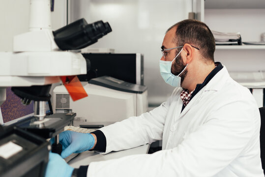 A senior biologist works with his computer and observes materials under a microscope. She is in a modern laboratory.