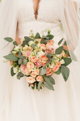 Wedding bouquet in pastel colors in the hands of the bride of roses, eustoma, peonies, carnations and eucalyptus.