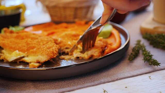 Fork and knife cutting a piece of juicy delicious cordon bleu steak - camera push in, slow motion, close up