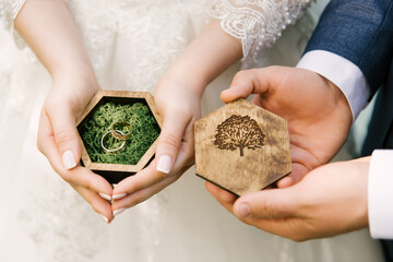 The hands of the bride and groom hold a wooden ring box, wedding rings