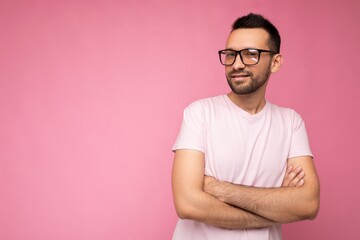 Handsome young happy brunet unshaven man wearing white t-shirt for mockup and stylish optical glasses isolated over pink background wall looking at camera