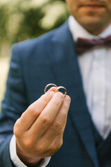 The groom holds 2 wedding rings in his hands