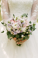 Wedding bouquet in pastel colors in the hands of the bride of roses, eustoma, peonies, carnations and eucalyptus.
