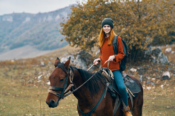 woman hiker with a backpack rides a horse in the mountains nature travel